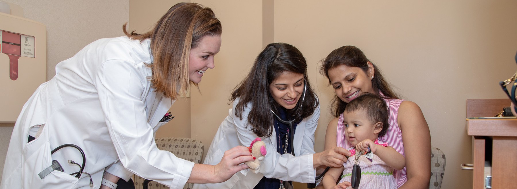 Med/Peds providers examine a child in a mother's lap.